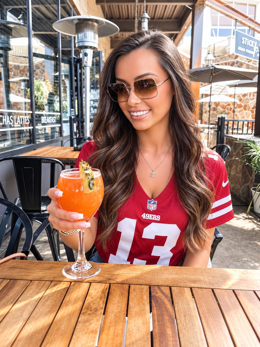 A guest in a red jersey holding up a tropical mimosa on a sunny patio