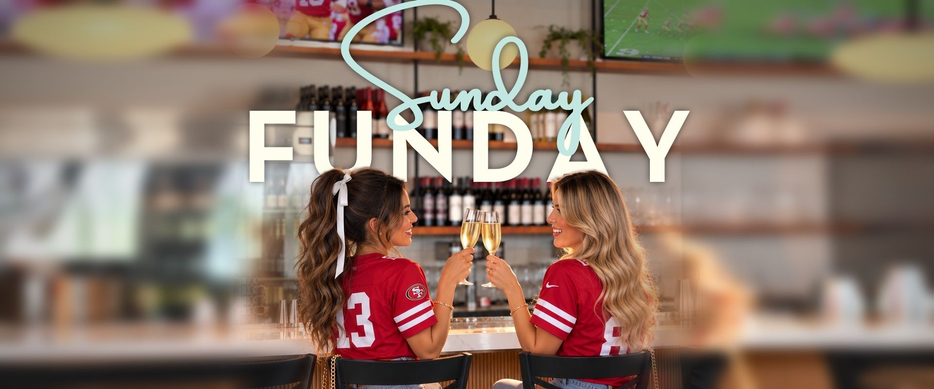 Sunday Funday: two friends in red football jerseys toasting with champagne at a Mimosa House bar, the game on the TVs behind them